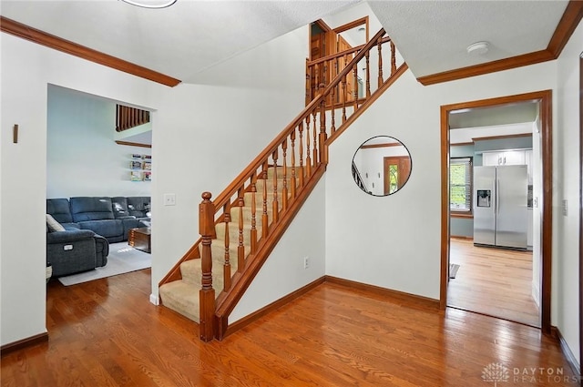 staircase with crown molding, baseboards, and wood finished floors