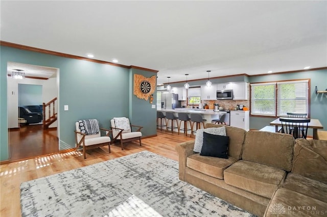 living room with crown molding, stairs, and light wood-style flooring