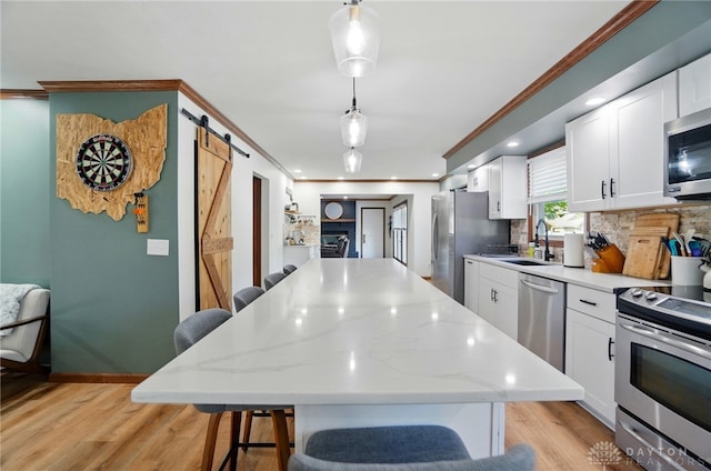 kitchen featuring a kitchen bar, crown molding, a barn door, a sink, and stainless steel appliances