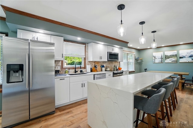 kitchen with white cabinets, a sink, stainless steel appliances, backsplash, and ornamental molding