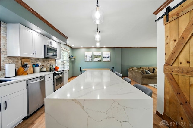 kitchen featuring backsplash, appliances with stainless steel finishes, white cabinets, light wood finished floors, and ornamental molding