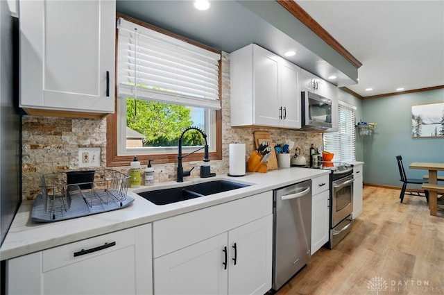 kitchen with ornamental molding, a healthy amount of sunlight, a sink, backsplash, and stainless steel appliances
