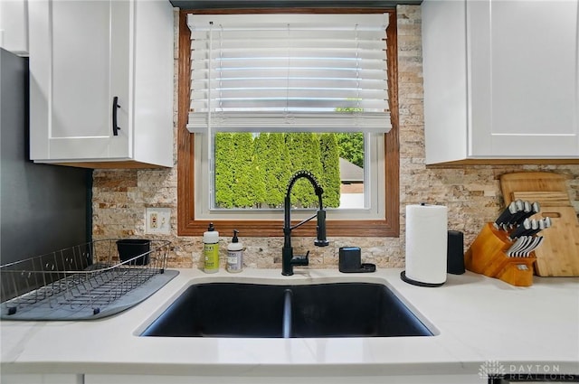 interior details with a sink, white cabinetry, backsplash, and light countertops