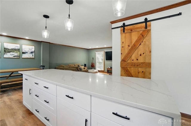 kitchen featuring hanging light fixtures, a barn door, light stone counters, white cabinetry, and light wood-type flooring