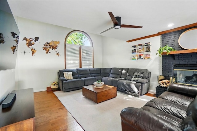 living area featuring a brick fireplace, a ceiling fan, baseboards, and wood finished floors