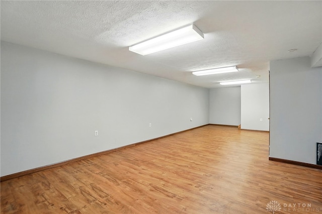 finished below grade area with a textured ceiling, baseboards, and light wood-type flooring