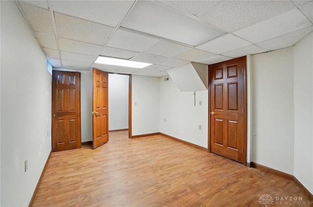 finished below grade area featuring baseboards, a drop ceiling, light wood-type flooring, and visible vents