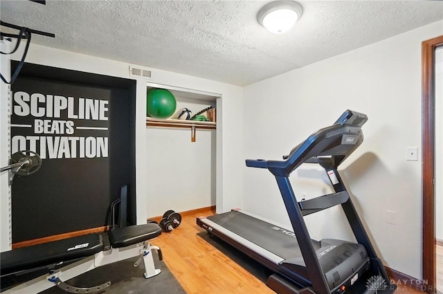 exercise room with a textured ceiling, wood finished floors, and visible vents