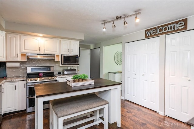 kitchen featuring decorative backsplash, dark wood-style flooring, white cabinetry, under cabinet range hood, and double oven range