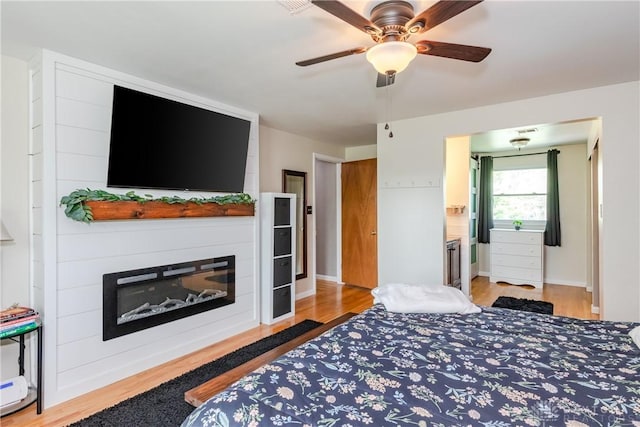 bedroom with baseboards, light wood-style flooring, ceiling fan, and a fireplace