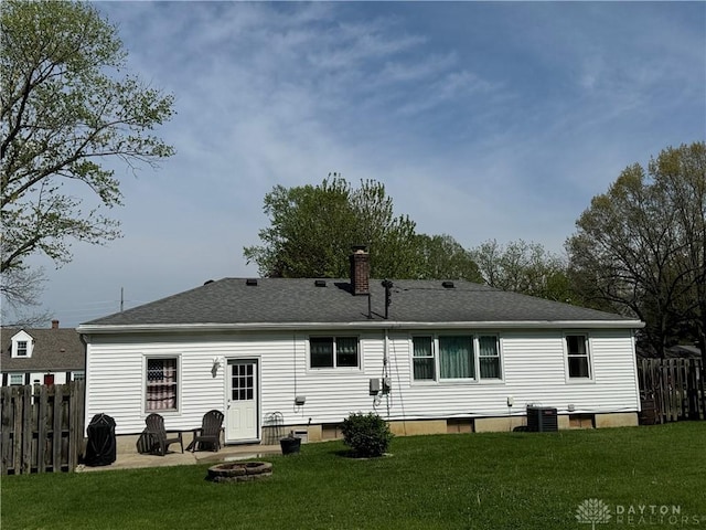 back of house featuring a chimney, a lawn, a shingled roof, fence, and a fire pit