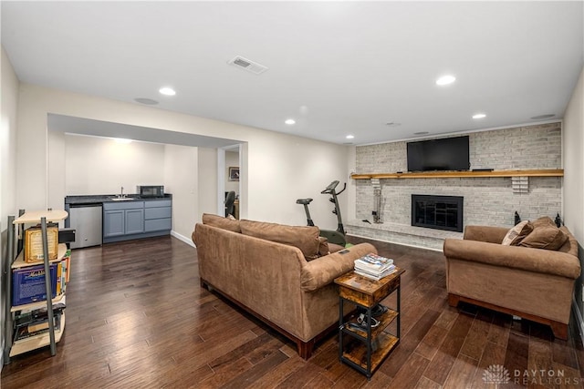 living area featuring dark wood-style flooring, a brick fireplace, recessed lighting, baseboards, and visible vents