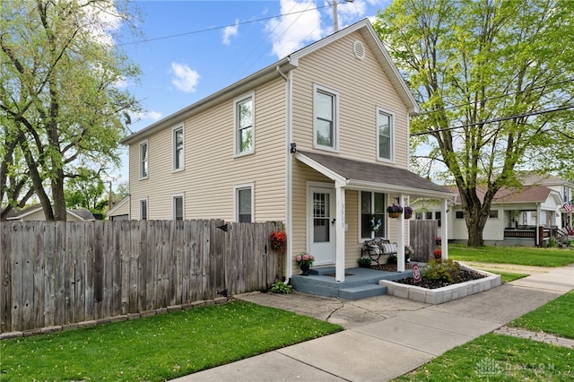 traditional-style house with fence, covered porch, and a front yard