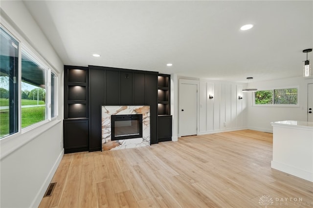 unfurnished living room featuring a premium fireplace, light wood-style flooring, recessed lighting, baseboards, and visible vents