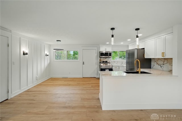 kitchen with appliances with stainless steel finishes, a sink, light countertops, a peninsula, and backsplash