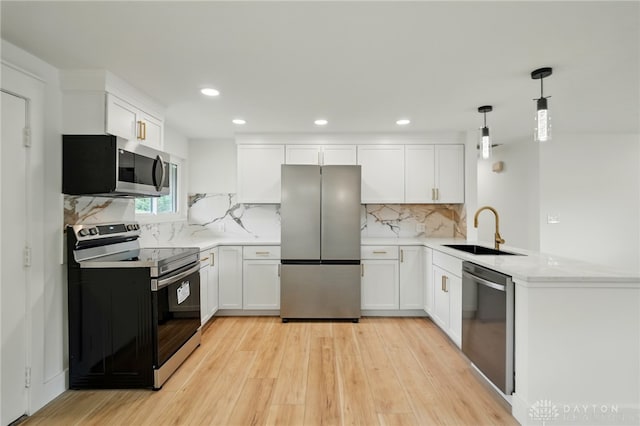 kitchen with light wood-style floors, a sink, appliances with stainless steel finishes, and a peninsula