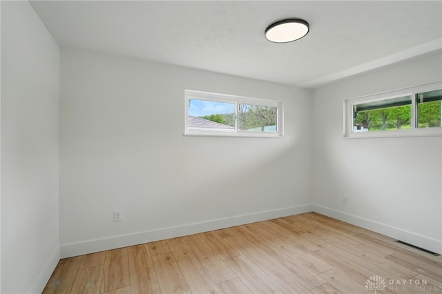 spare room with baseboards, plenty of natural light, and light wood finished floors