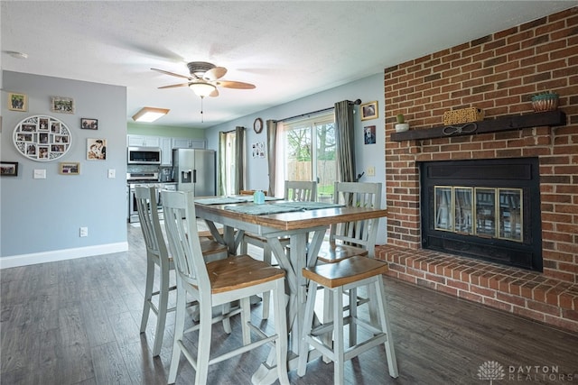 dining room featuring baseboards, a fireplace, a ceiling fan, and wood finished floors