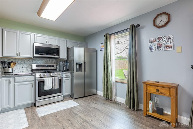 kitchen with appliances with stainless steel finishes, baseboards, backsplash, and light wood finished floors