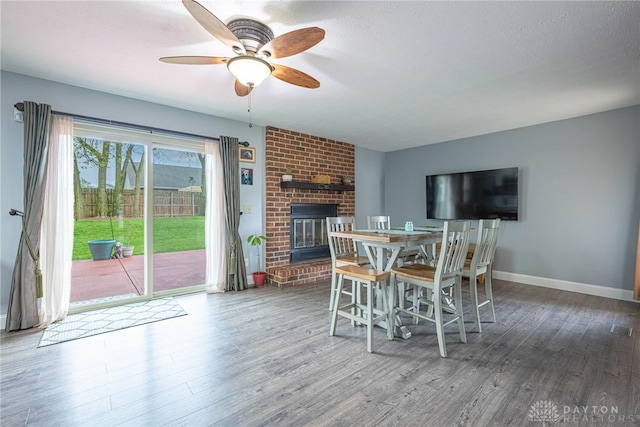 dining area with a brick fireplace, a ceiling fan, baseboards, and wood finished floors