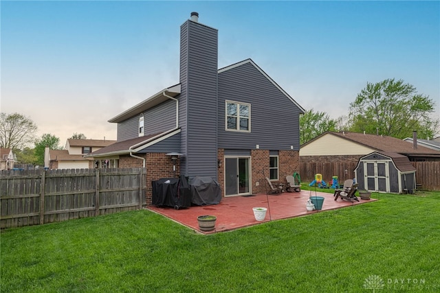 back of house with a storage shed, a lawn, a patio area, and brick siding