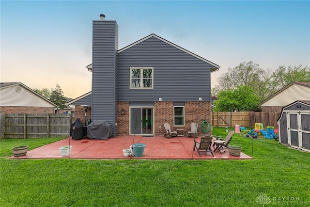 back of house at dusk with a storage shed, a fenced backyard, a patio area, and an outdoor fire pit