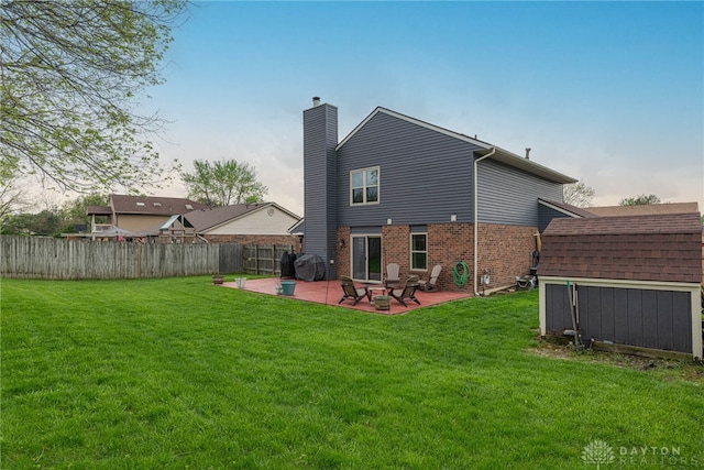 back of house with a chimney, a patio area, brick siding, fence, and a yard