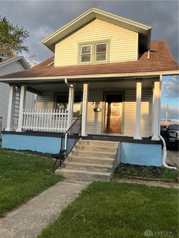 view of front of home with a shingled roof, a porch, and a front lawn