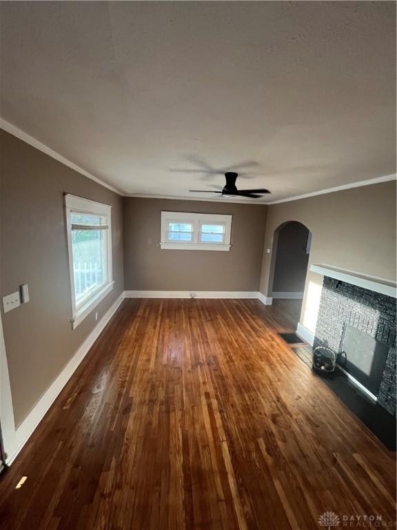 unfurnished living room with a ceiling fan, dark wood-style flooring, crown molding, arched walkways, and baseboards
