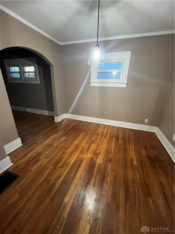unfurnished dining area featuring baseboards, arched walkways, wood-type flooring, and ornamental molding