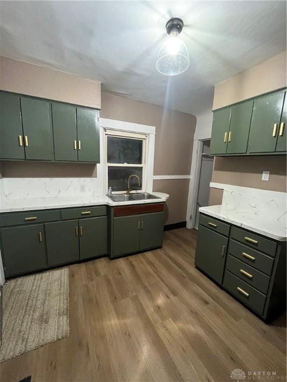 kitchen featuring light countertops, green cabinetry, a sink, and wood finished floors