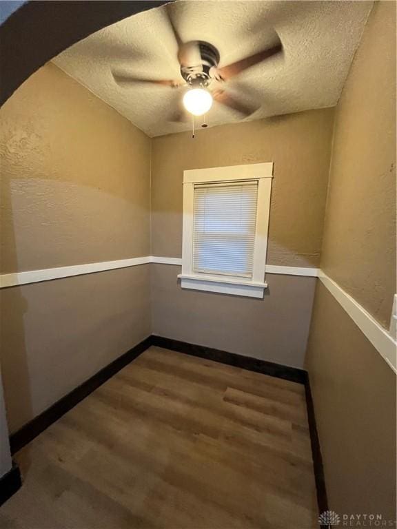 empty room with baseboards, a ceiling fan, a textured ceiling, and wood finished floors