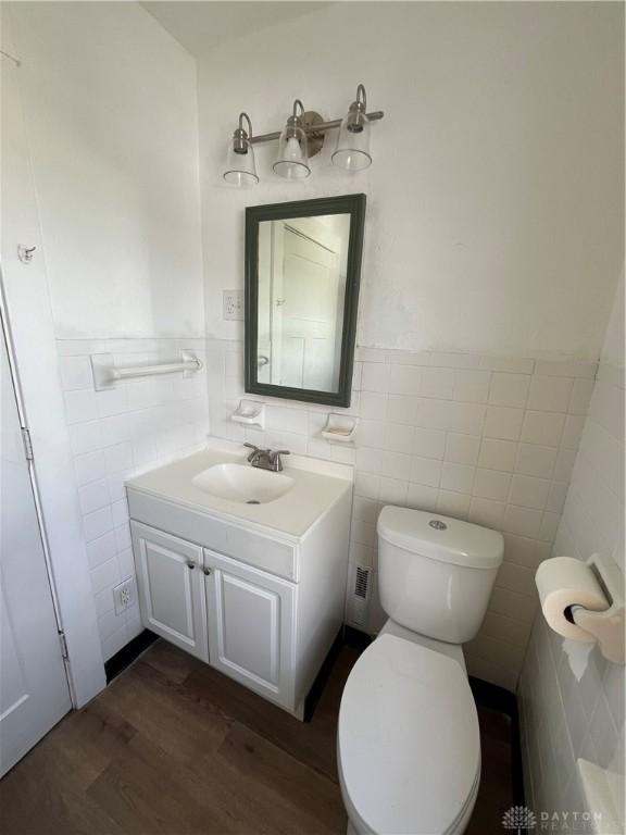 bathroom featuring vanity, toilet, a wainscoted wall, tile walls, and wood finished floors