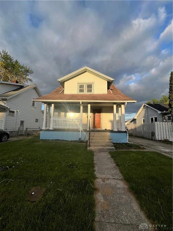 bungalow-style house featuring covered porch, fence, and a front lawn