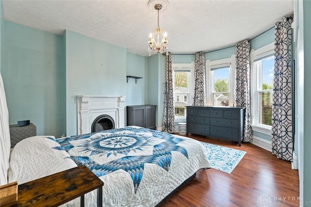 bedroom with baseboards, a notable chandelier, wood finished floors, and a fireplace