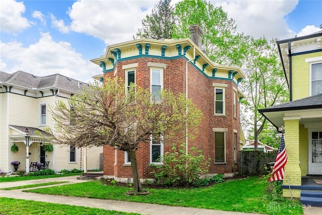italianate house featuring a chimney, a front lawn, and brick siding