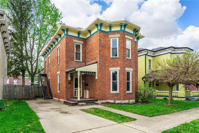 italianate home featuring brick siding, a front lawn, fence, and driveway