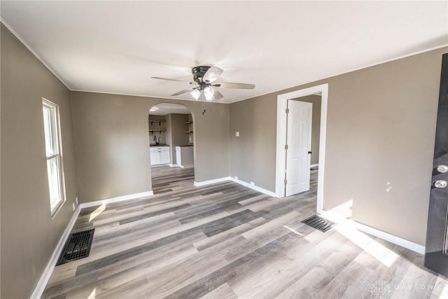 spare room with arched walkways, a ceiling fan, baseboards, wood finished floors, and visible vents