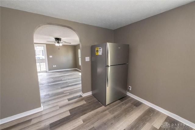 kitchen with arched walkways, freestanding refrigerator, a ceiling fan, baseboards, and wood finished floors