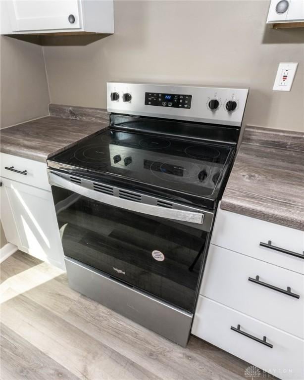kitchen with stainless steel electric stove, white cabinets, and light wood-style floors