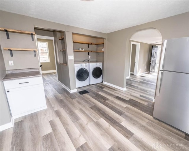 laundry room featuring arched walkways, laundry area, washing machine and dryer, and light wood finished floors