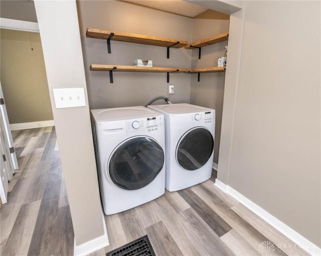 washroom with washing machine and clothes dryer, baseboards, and light wood finished floors
