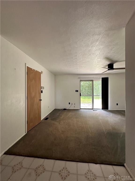 carpeted empty room featuring baseboards, a textured ceiling, and tile patterned floors