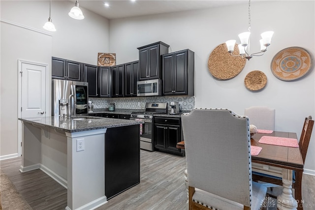 kitchen featuring backsplash, a notable chandelier, dark stone counters, stainless steel appliances, and light wood-style flooring