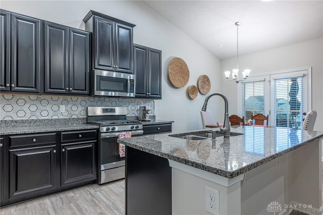 kitchen featuring dark cabinetry, appliances with stainless steel finishes, stone counters, and a sink