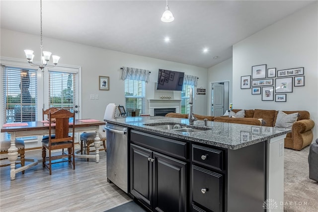 kitchen featuring an inviting chandelier, stainless steel dishwasher, open floor plan, dark cabinetry, and a sink