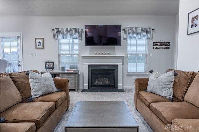 carpeted living area featuring baseboards, a fireplace with flush hearth, and a healthy amount of sunlight