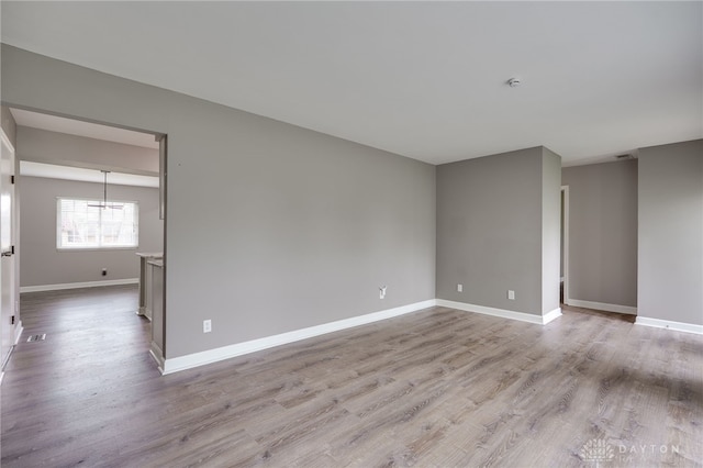 empty room featuring baseboards, a notable chandelier, and wood finished floors