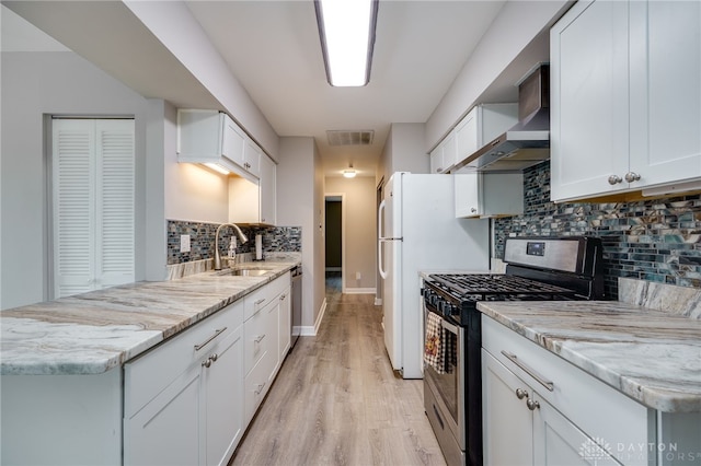 kitchen featuring wall chimney range hood, appliances with stainless steel finishes, tasteful backsplash, light wood-type flooring, and a sink