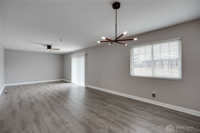 spare room with baseboards, visible vents, wood finished floors, and ceiling fan with notable chandelier